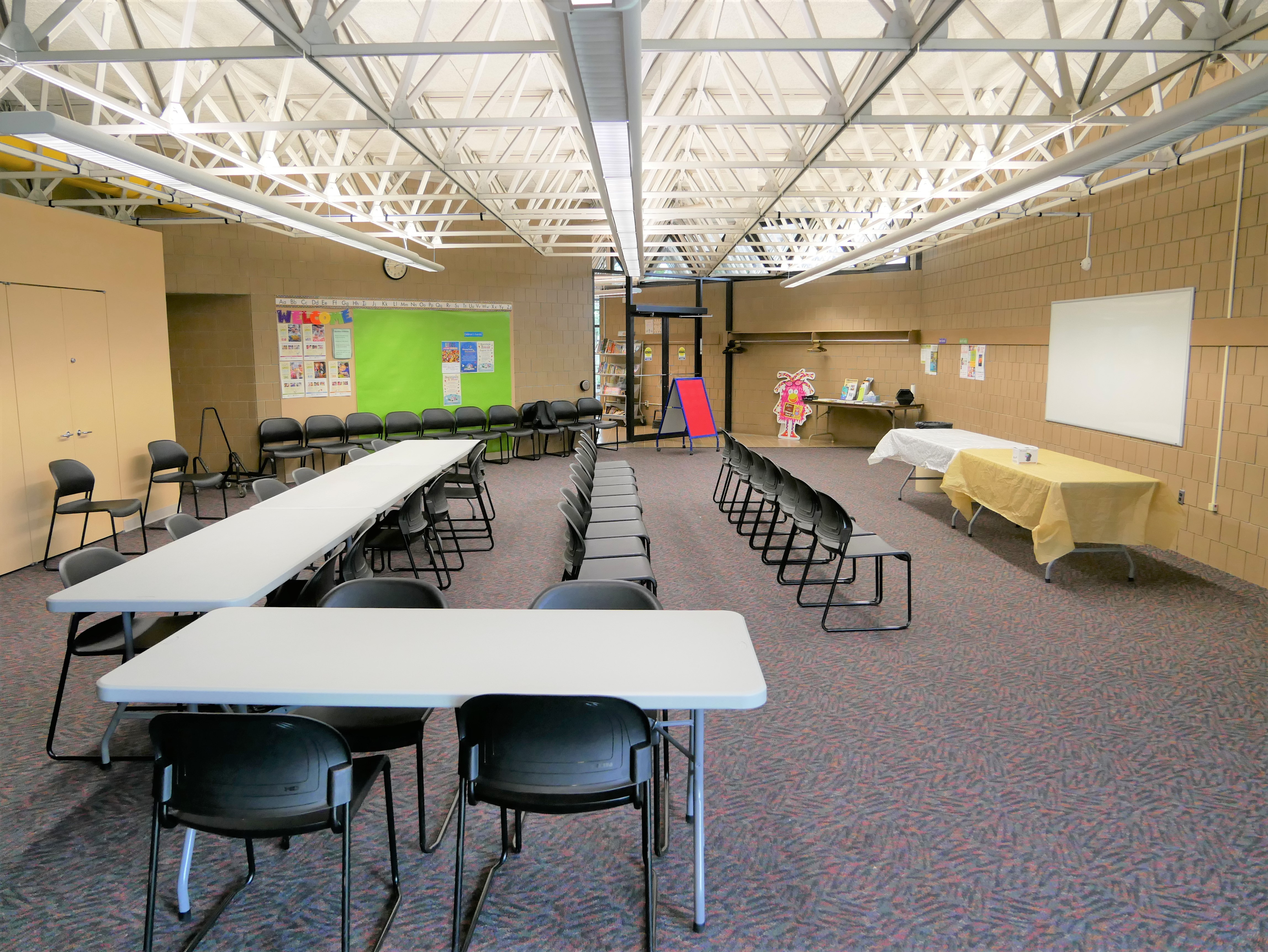 South Side Library Meeting Room with tables arranged in an L-shape, free standing chairs spread out in rows, and a whiteboard at the front of the room