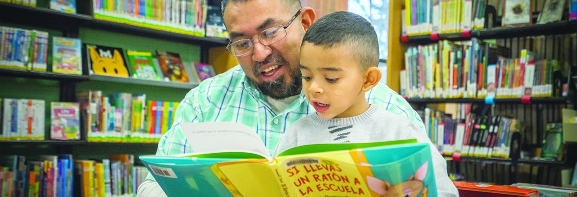 Father reading with his young son in the children's area of the library