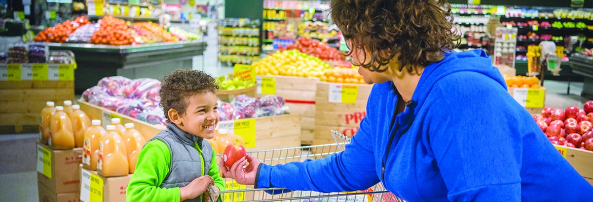 Woman holding a tomato in the grocery store and talking to her young son