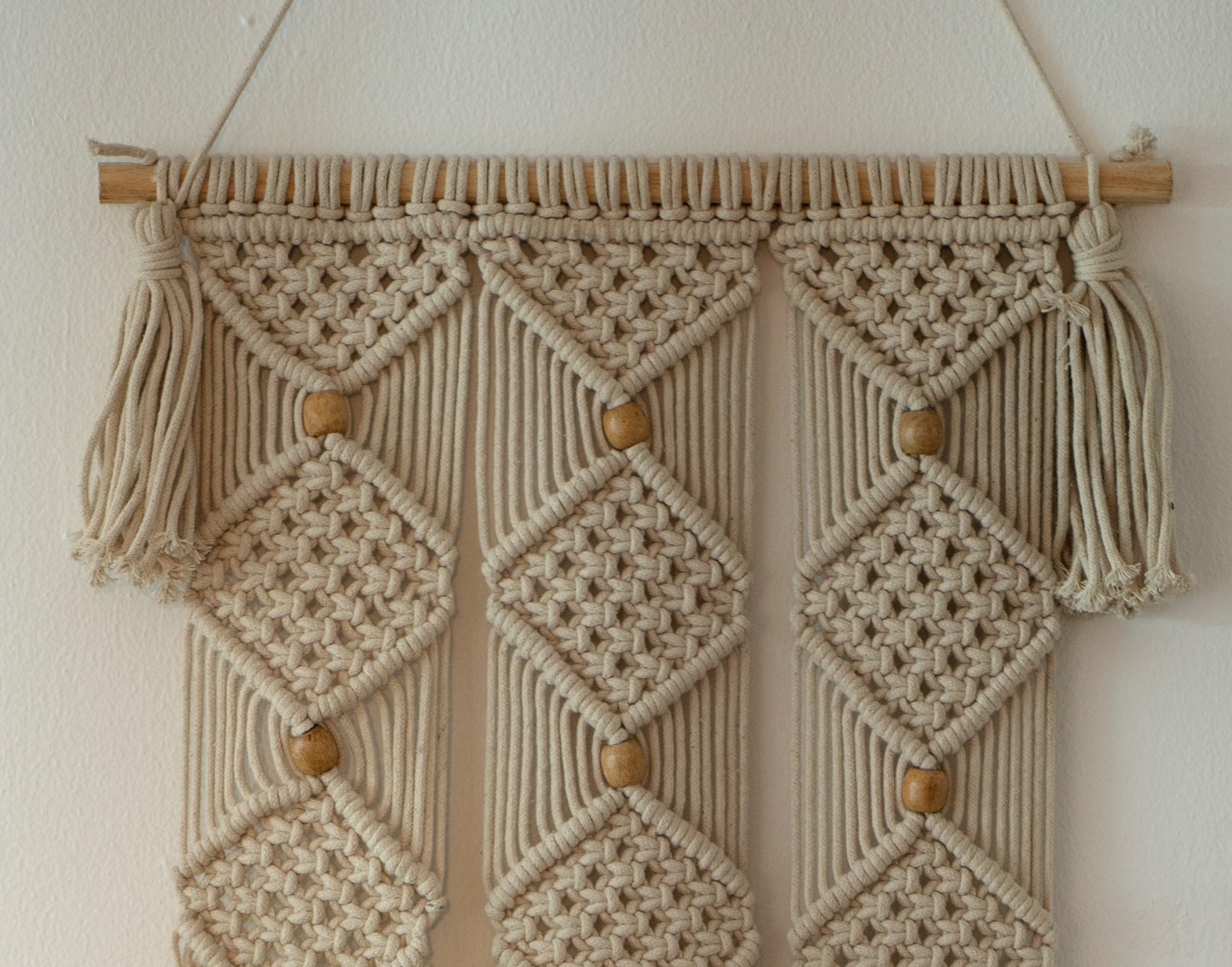 Tan macramé project hanging on a white wall 