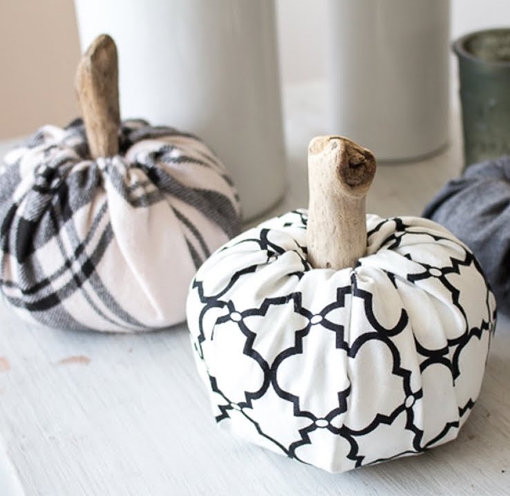 Craft pumpkins made of fabric and sticks sitting on a white table.