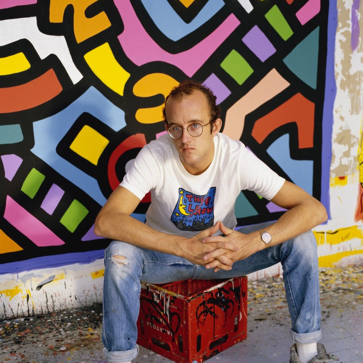 man sitting on red crate in front of a colorful painting