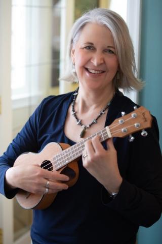 A blond woman smiling and holding her ukulele