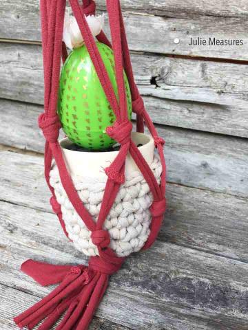 white plant holder suspended in from of a wooden wall by a red macrame project