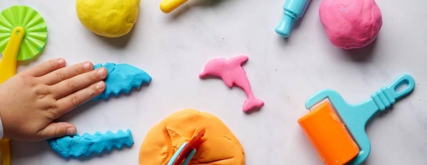 A hand playing with various colors of playdough, as well as tools like a roller and rolling pin.