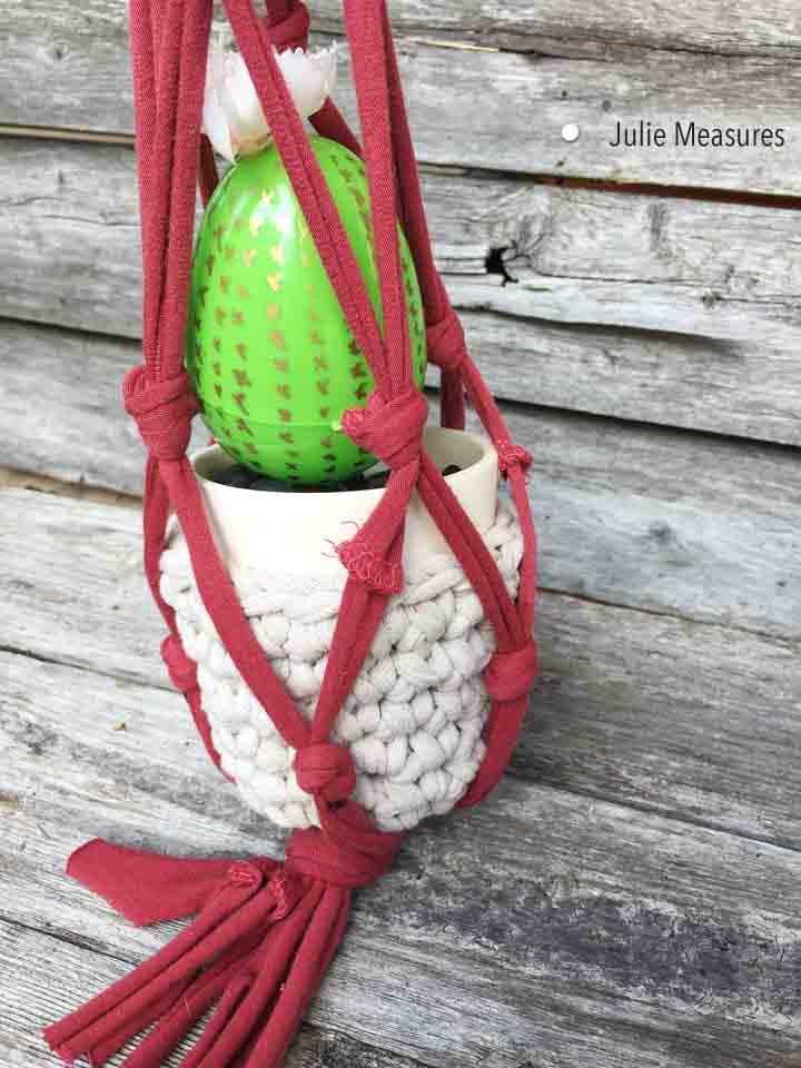 white plant holder suspended in from of a wooden wall by a red macrame project